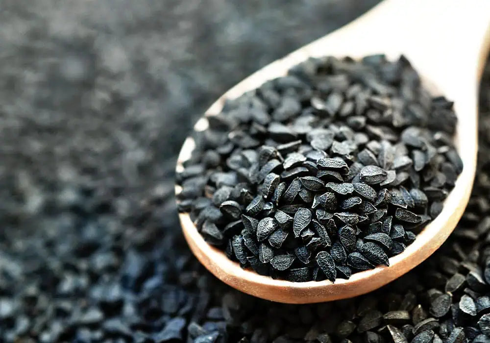 Eine Holzlöffel mit schwarzen Samen liegt auf einer dunklen Fläche. Die Samen haben eine ovale Form und sind glänzend. Ideal für die Verwendung in Nahrungsergänzungsmitteln.